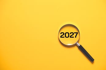 the year 2027 inside of a magnifying glass on a bright yellow background