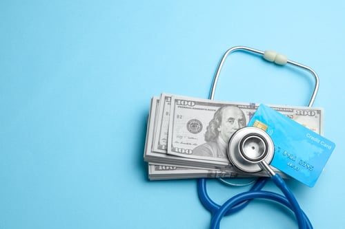 Stack of cash dollars and credit card under a stethoscope on blue background
