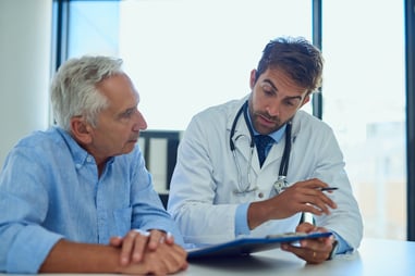 A male doctor going over paperwork on a clipboard with a male senior patient in a medical clinic.