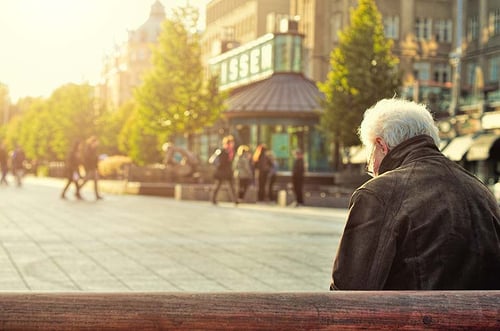 senior man sitting on a bench outside at sunset