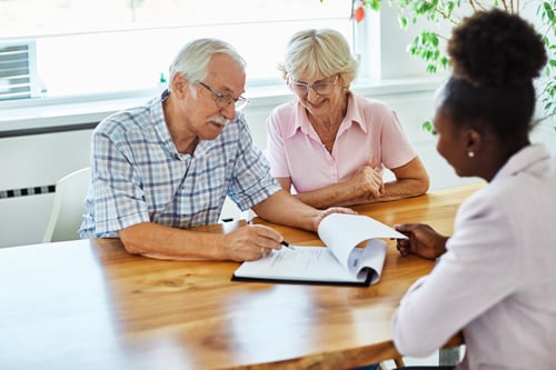 happy senior couple meeting with insurance advisor on insurance plans signing paperwork on wood table