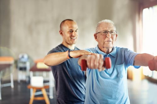 a senior man wearing glasses holding hand weights performing PT with a physical therapist