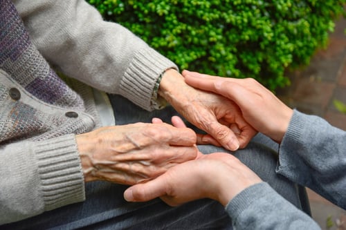 young hands holding elderly hands in lap of senior