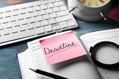 pink sticky note with deadline reminder on a notebook near keyboard on desk