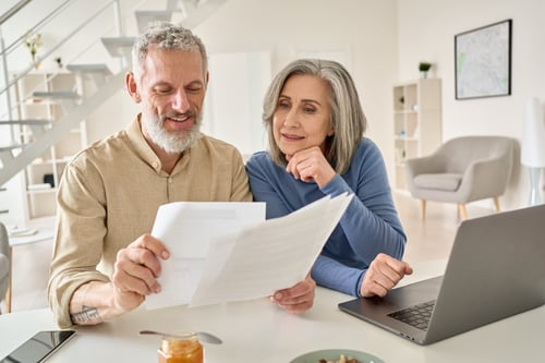 a senior couple sitting at a table in living room looking at important paperwork together