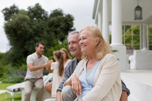senior couple sitting outdoors with family in the background