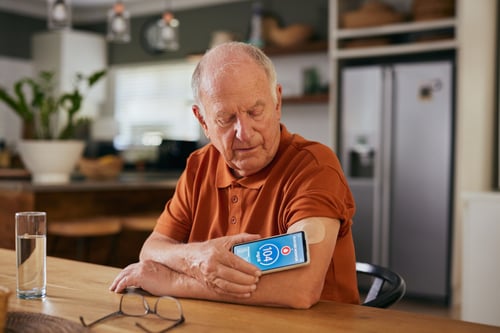 senior man with diabetic chronic condition checking blood sugar levels with smart smartphone connected to a continuous glucose monitor