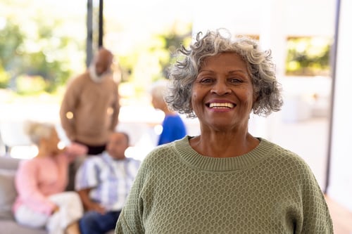 Portrait of smiling african american senior woman in green sweater standing with friends in background