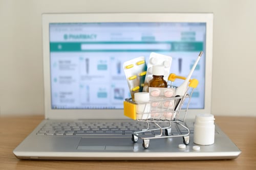 small toy shopping cart full of medications sitting on top of a laptop