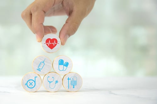 hand holding wooden circle block over a stack each with a different medical picture icon to represent various healthcare needs