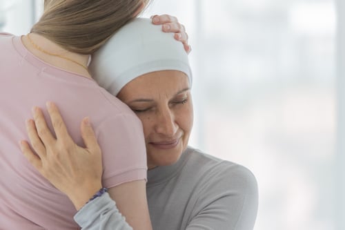a middle aged woman with cancer wearing head covering hugging a female family member