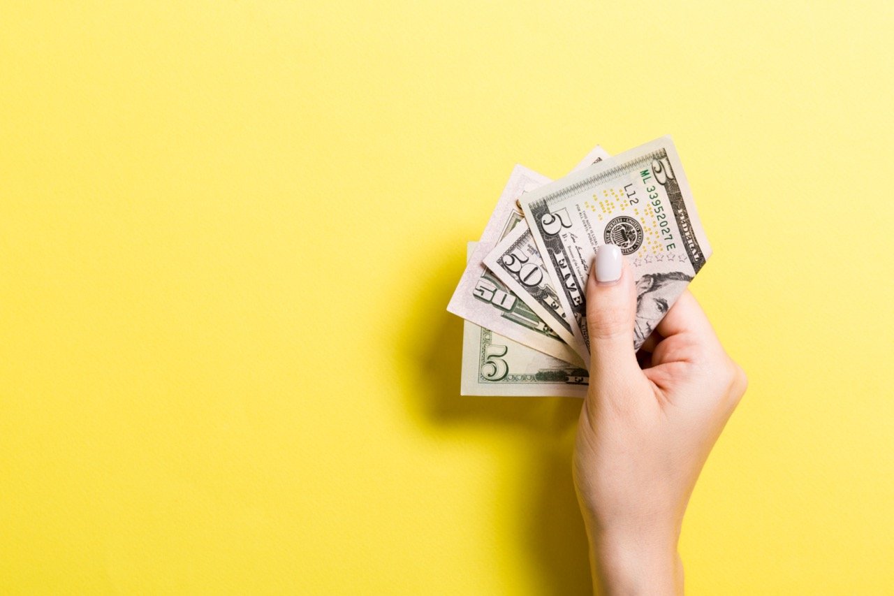 female hand holding cash giveback in front of yellow background